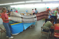 Women holding up three rugs that have not been cut apart yet.