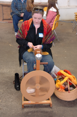 Spinner wearing colorful shawl spinning on Kiwi wheel.